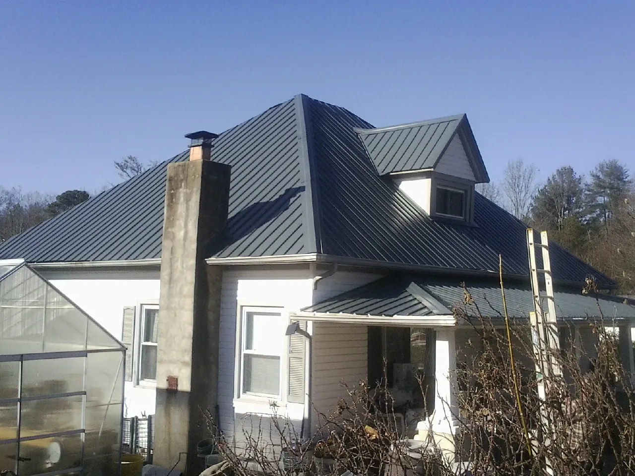 Dark blue standing seam metal roof on a white farmhouse with dormer — Slate & Tile Roof Repair by Roofing Brothers in Snowmass Village