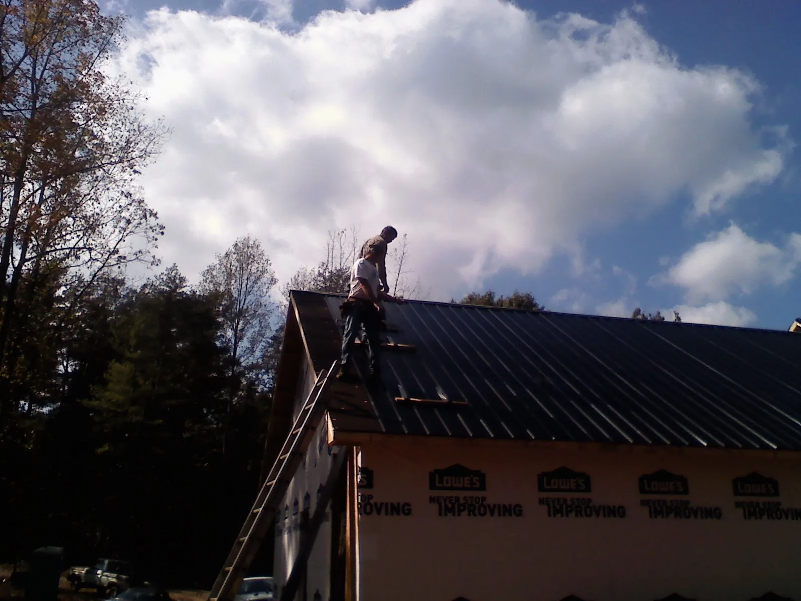 Roofer fastening dark metal panels high against a cloudy sky, from a Roof Inspection job in Snowmass Village